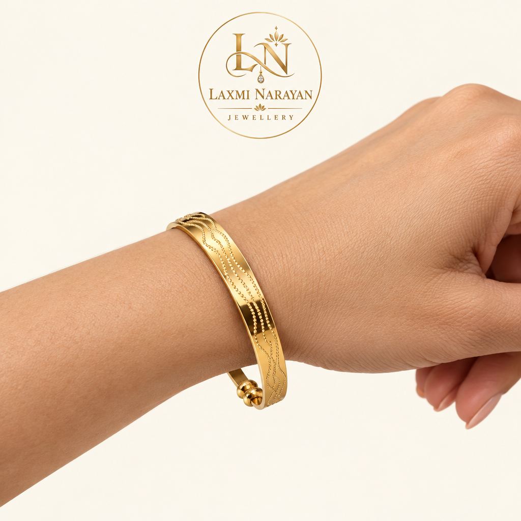 Woman's wrist wearing a single gold-tone kada with brand logo